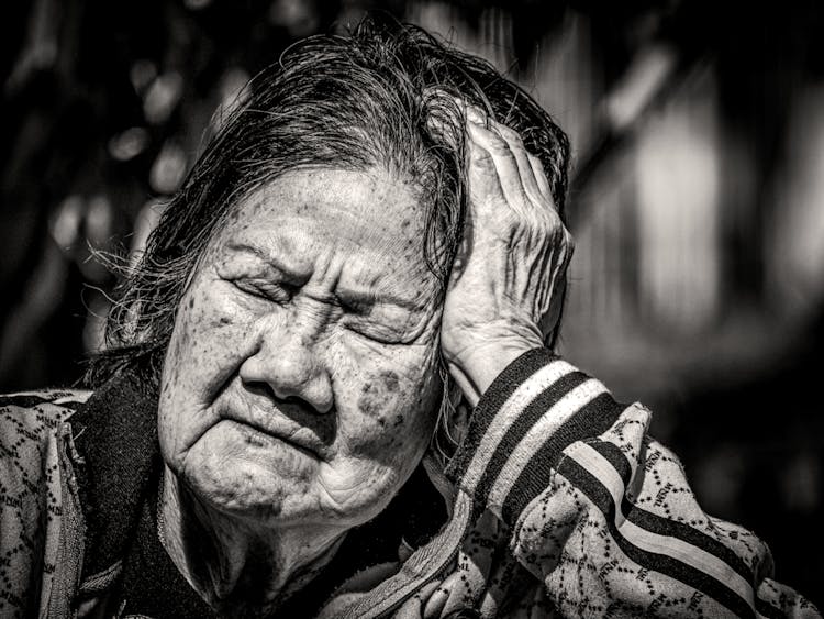 一位老妇人闭着眼睛坐在阳光下的黑白照片