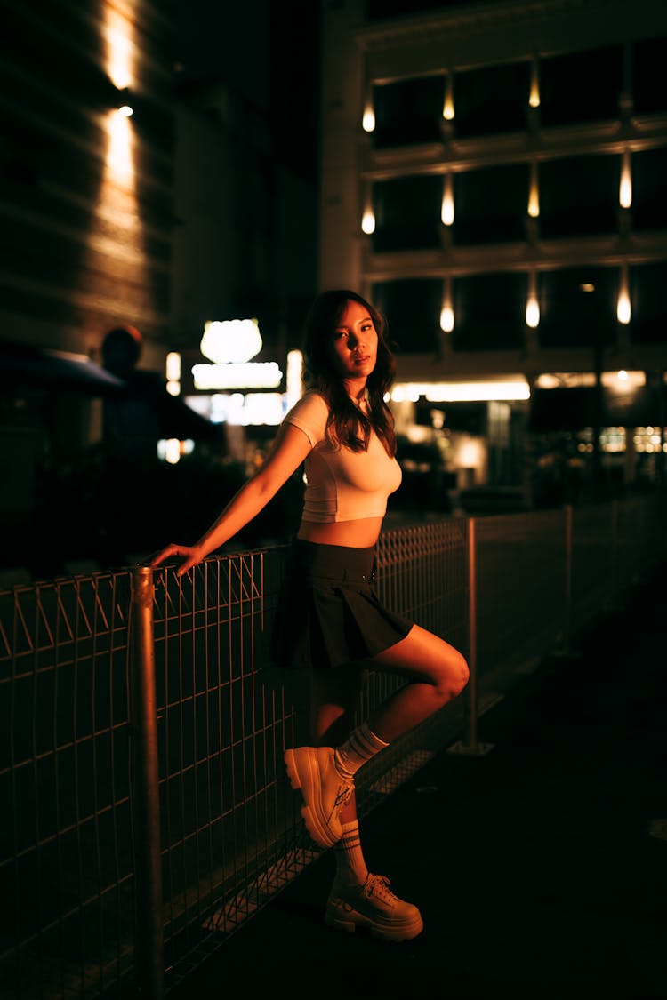 穿着露脐上衣和裙子的年轻女子站在城市的栅栏旁