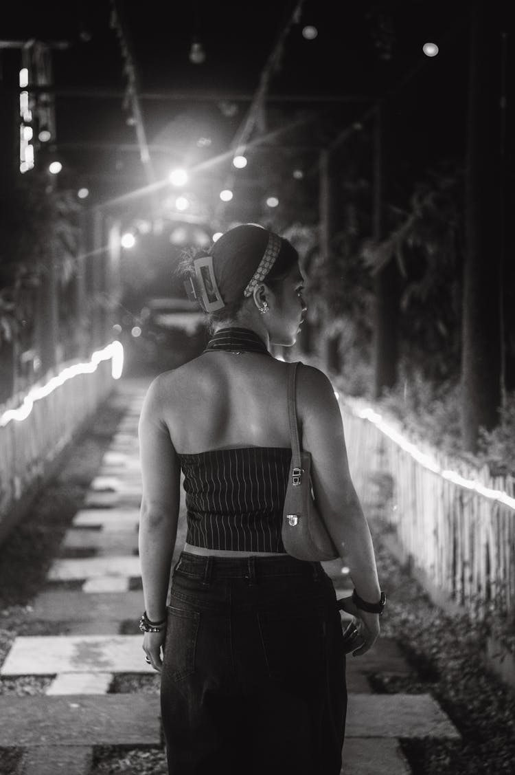 黑发女人在花园的人行道上穿着黑色裤子和手提包