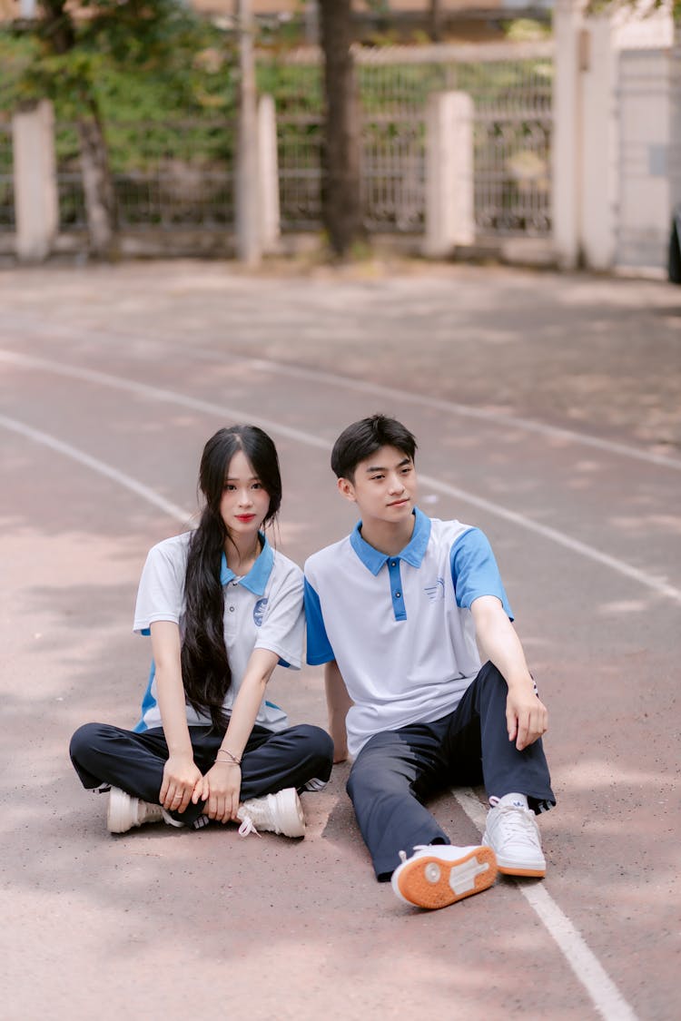 一个穿着运动服的年轻男孩和女孩坐在跑道上