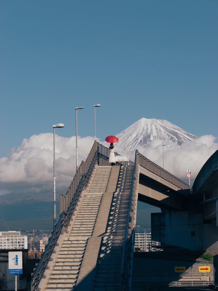 手持红伞的女子站在富士山背景的高架步道台阶上