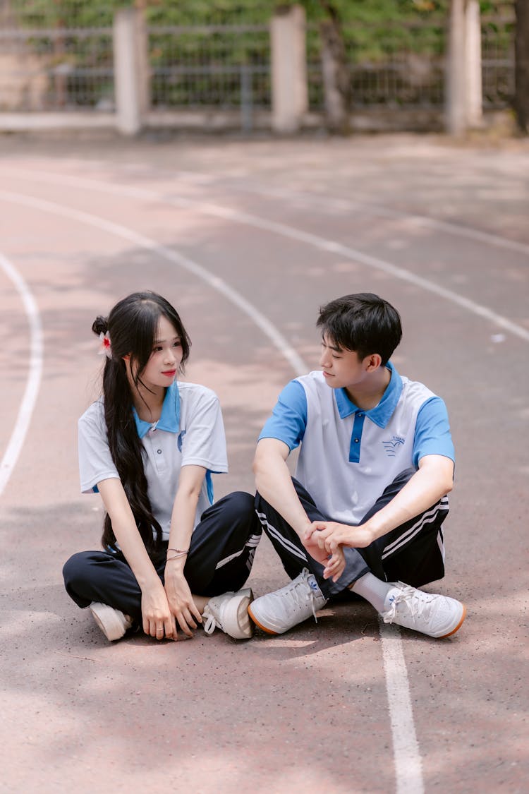 一个穿着运动服的年轻男孩和女孩坐在跑道上
