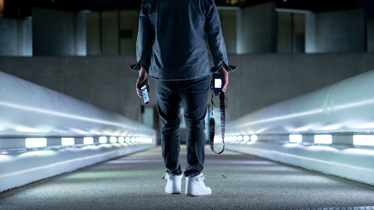 一名男子手持智能手机和数码相机站在人行天桥上