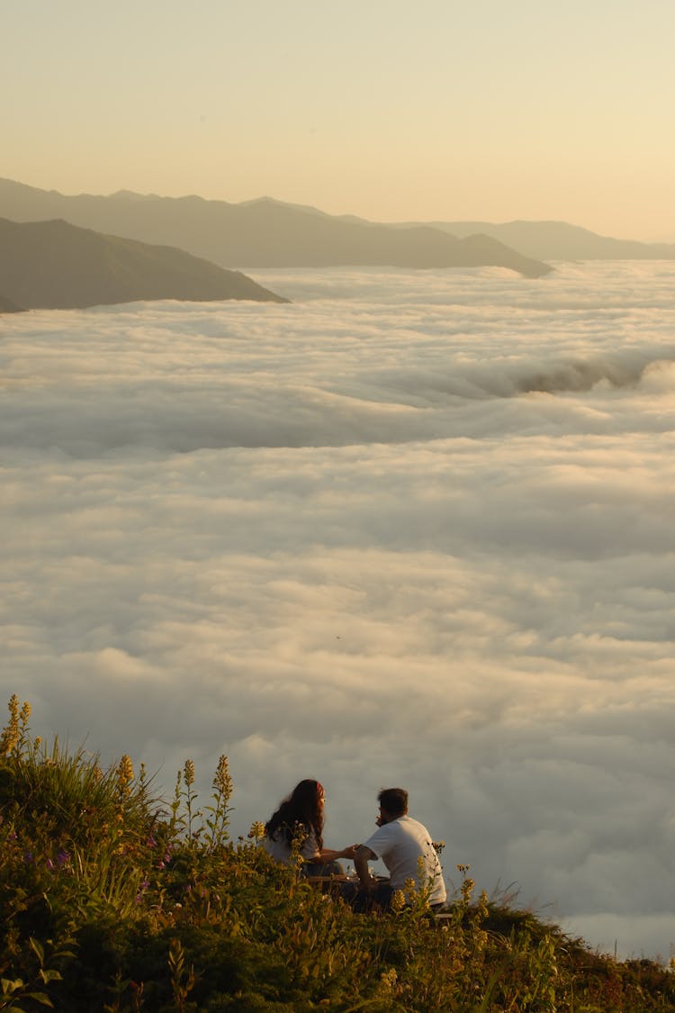 情侣坐在山上，下面有云